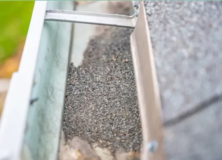 Shingle grit and roof sand washed into a gutter — gutter guards block shingle grit and sediment