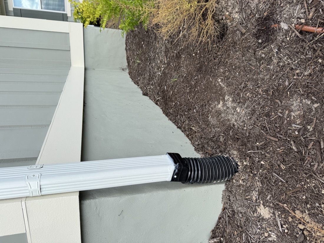 Seamless gutter downspout draining away from a Fleming Island home's foundation